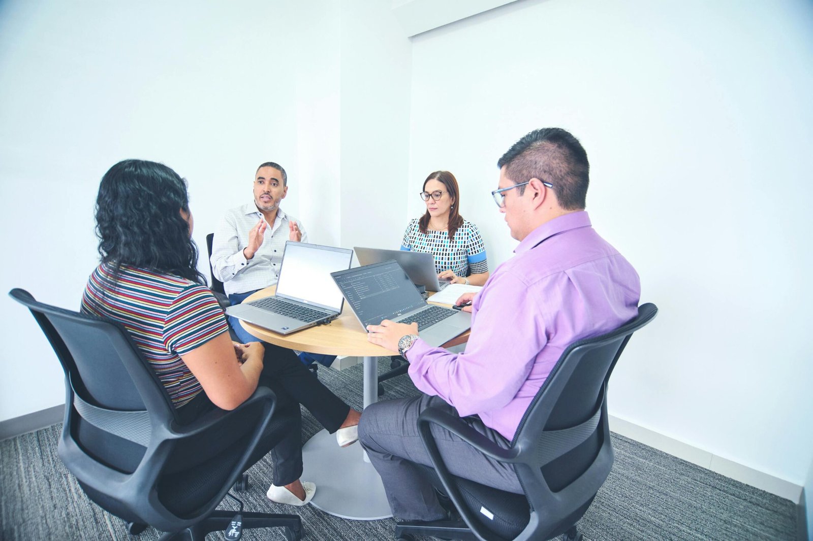 Diverse team engaged in a corporate meeting with laptops in a bright, modern office setting.